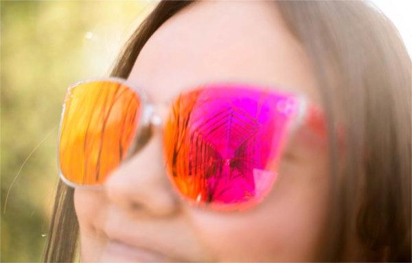  A person wearing pink and orange sunglasses smiles.