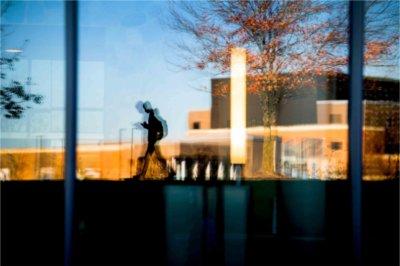 The silhouette of a student walking with their phone is reflected into glass windows.