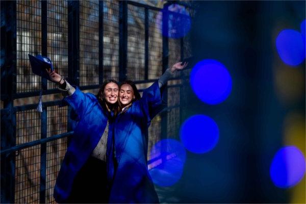  Students celebrate with graduation caps and gowns near blue lights.