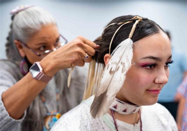  An Indigenous dancer receives help with regalia before a Powwow Ceremony.