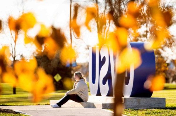  A person is pictured at the Laker Letters with yellow and orange autumn tree colors.