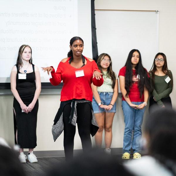 Students stand at the front of a classroom and give a presentation.