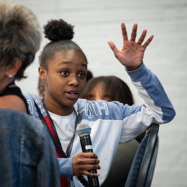 A student waves her hand as she speaks into a microphone