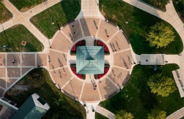 A drone photo looking straight down on the carillon tower of a campus community as students walk past. 