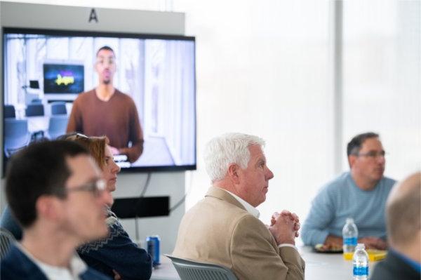 GVSU faculty watch the national convening video. A screen with the video plays behind two people. 