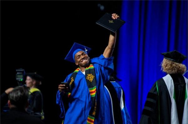 A student proudly holds his diploma up as he crosses the stage during graduation.