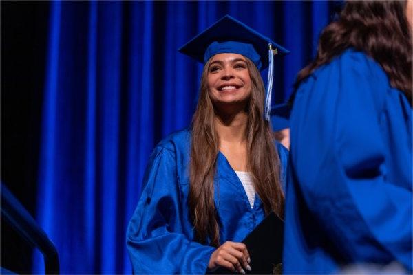 Graduating student Larissa Hollingsworth smiles at her family in the crowd as she receives her diploma.