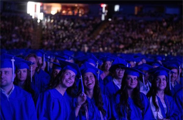 Graduates smile as they watch a video playing on the big screen at Commencement.