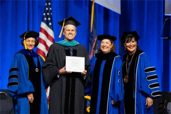 GVSU officials pose and smile with guest speaker Timothy Shriver, who received an honorary degree. 