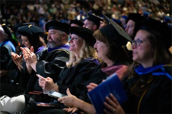 Faculty and Staff smile and clap in the audience during Commencement.