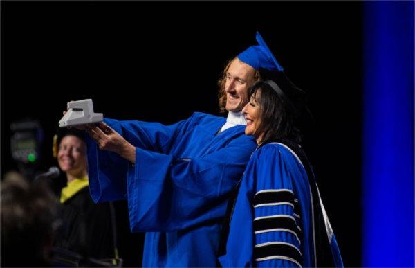 A graduate takes a selfie with President Mantella as he crosses the stage at Commencement.