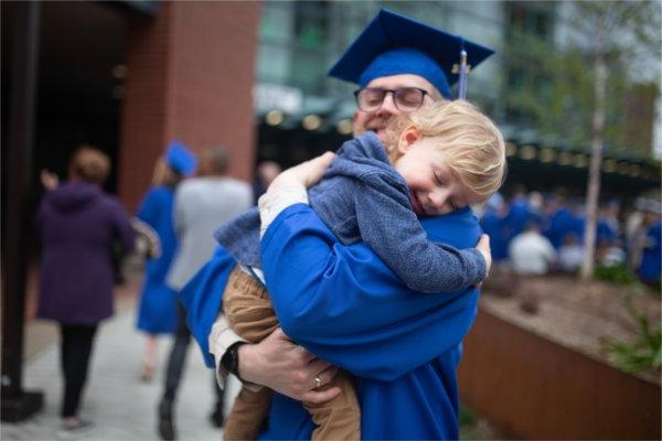 A graduate hugs a young child tight following Commencement ceremonies. 