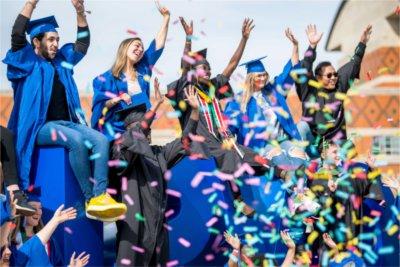 Graduates in their caps and gowns sit atop the Laker Letters and throw confetti in celebration.