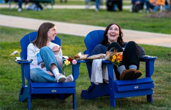  Two college students laugh together as they sit in blue Adirondack chairs.