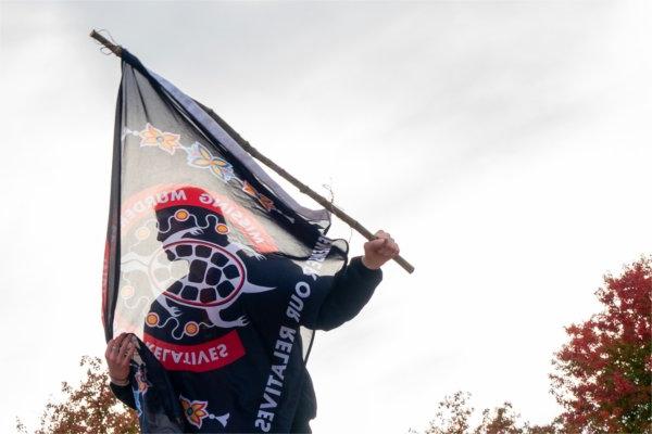  A student is silhouetted through a red and black flag they are carrying. 