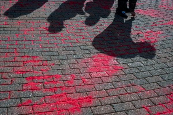  Shadows of students crouched over are cast on bricks with red sand being poured in the cracks. 