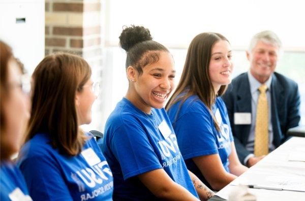  A row os smiling students wearing blue T-shirts talk with each other. 