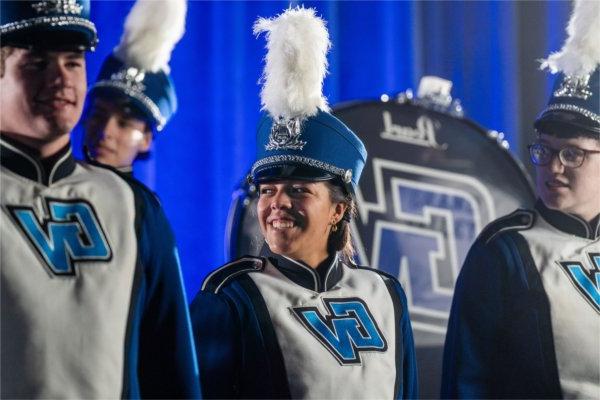  A college student wearing a band uniform with the letters GV on the front smiles with others. 