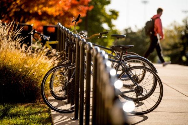  A student wearing a backpack walks past a row of bicycles in a bike rack. 