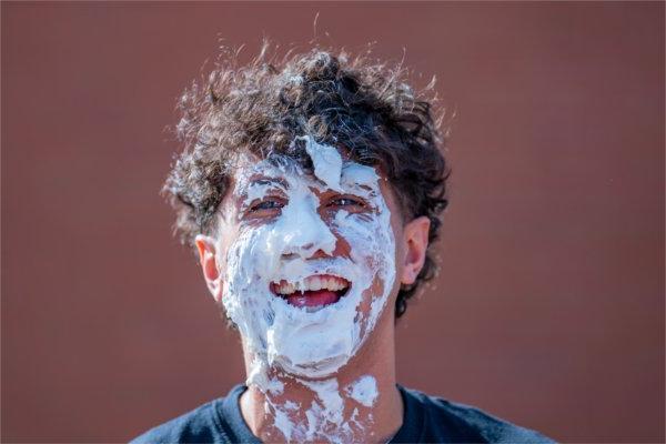 A college student laughs after having a pie thrown in their face. 