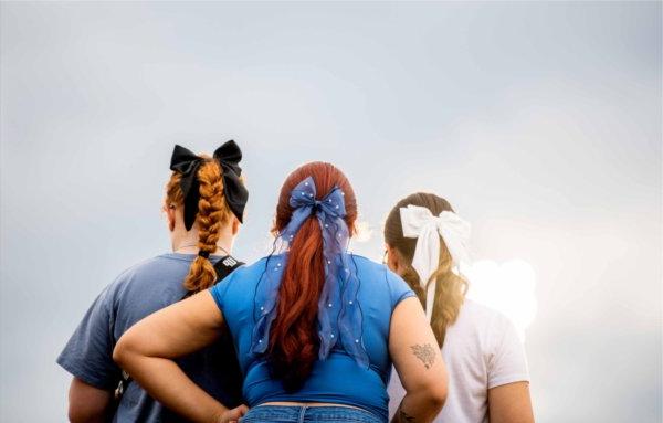  A detail of three college students with white, blue and black bows in their hair. 