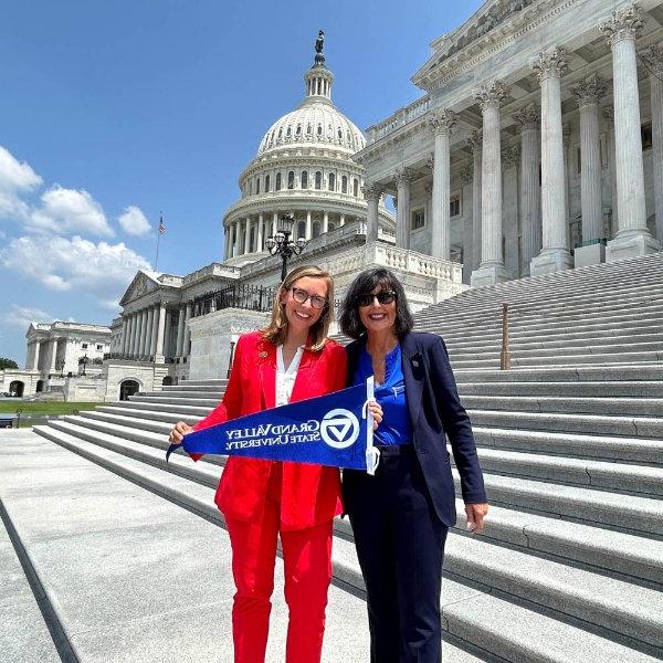 President Mantella and Representative Hillary Scholten stand on the Capitol steps together and hold a GVSU flag.