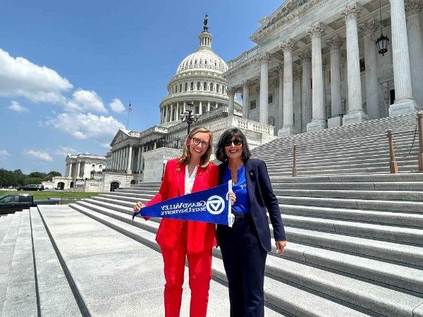 President Mantella and Representative Hillary Scholten stand on the Capitol steps together and hold a GVSU flag.