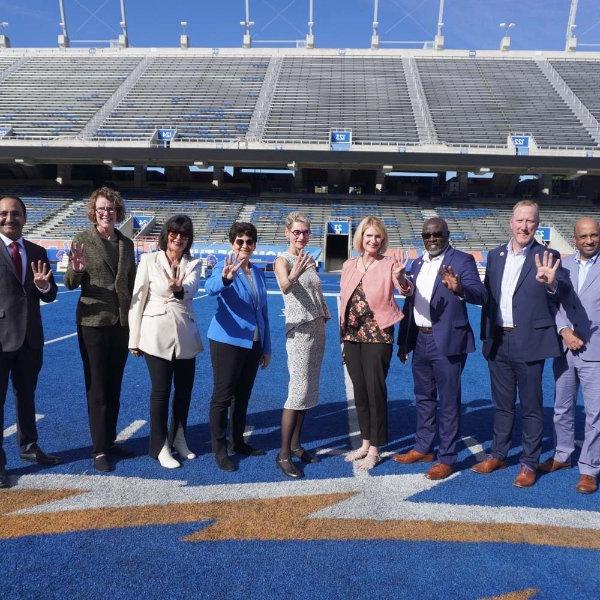 President Mantella and other rep 4 leaders pose for a photo on a blue football field. They all hold 4 fingers up.