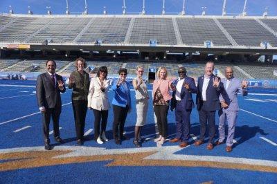 President Mantella and other rep 4 leaders pose for a photo on a blue football field. They all hold 4 fingers up.