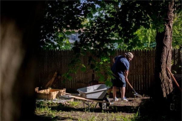 student with rake clearing weeds in a backyard with trees on left 