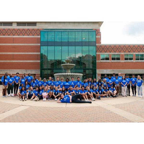 large group of students, faculty and staff members dressed in blue t-shirts and posing in front of the Student Services Building fountain