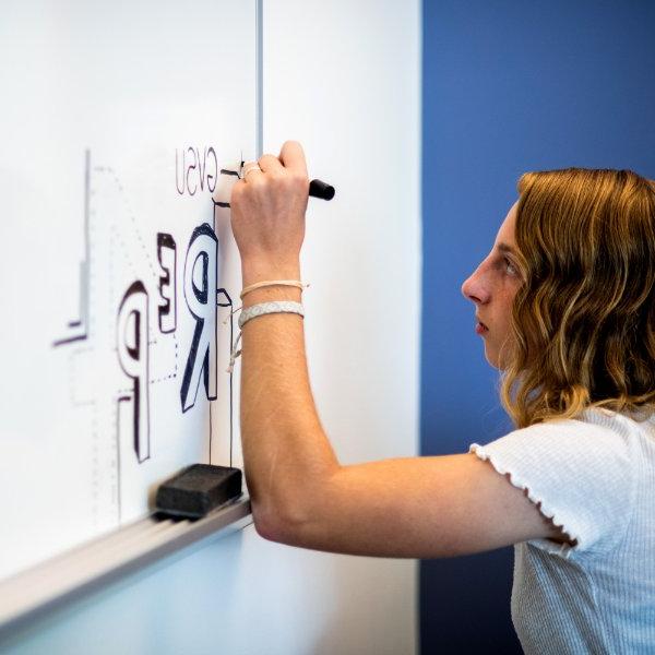 A student draws on a whiteboard with the words GVSU and REP4.