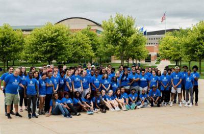 large group of students, faculty and staff all wearing blue GVSU Oliver Wilson Scholar t-shirts; pictured with Student Services Building behind them